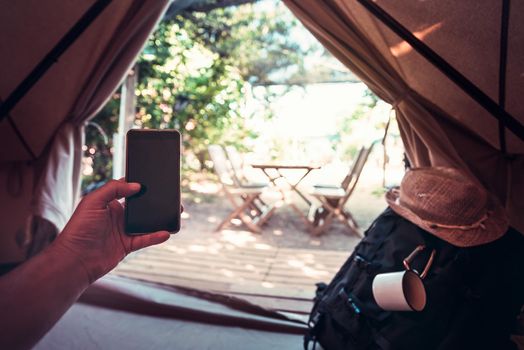 view of a hand of a hiker person resting while consulting the phone in a camping tent, travel discovery concept, point of view shot