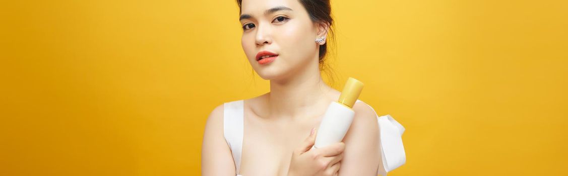 Portrait of Asian woman holding beauty product over yellow background