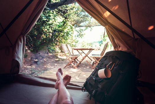 view of crossed feet of a hiker person resting barefoot in a camping tent, travel discovery concept, point of view shot