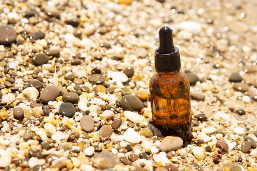 Cosmetic serum for the skin in a glass bottle. A bottle with an eyedropper on a pebble beach by the sea. Essences for skin care on the background of stones. The concept of natural cosmetics and SPA products.