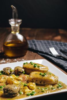 vertical photo of healthy traditional spanish hake dish with green seafood sauce with clams, prawns, green peas and egg, typical mediterranean cuisine with rustic dark food style