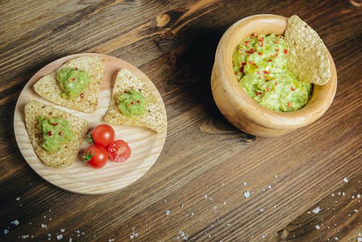 top view of guacamole in a wood bowl with nachos, typical mexican healthy vegan cuisine with rustic dark food photo style