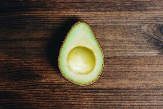 top view of half avocado without bone on wooden table, healthy vegan cuisine concept with rustic dark food photo style