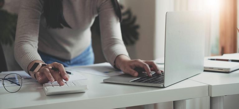 Finance Concept. Woman hold a graph pen, press a calculator and make money by writing reports, and memos, and analyzing business documents with a laptop computer vertically..