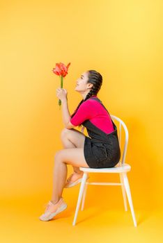Portrait of happy beautiful Asian woman with bouquet of flowers on yellow background