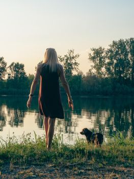 Beautiful woman enjoys holidays at sunset near river with pets company