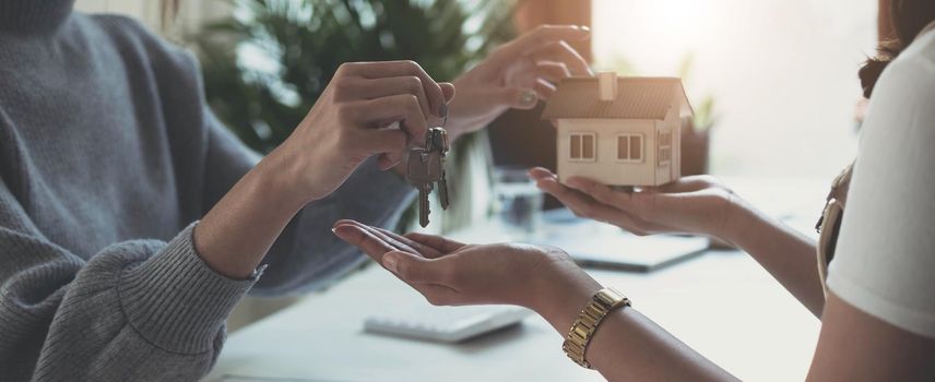 estate agent giving house keys to woman and sign agreement in office.