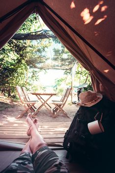 vertical view of crossed legs of a hiker man resting barefoot in a camping tent, travel discovery concept, point of view shot