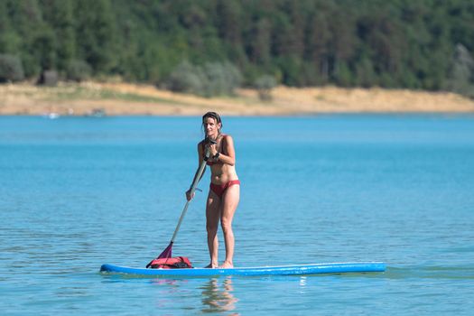 Woman Paddle Surfing on Lake Montbel in Ariege with the boats in the summer of 2022.