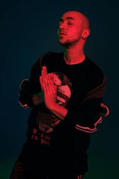 Close-up studio shot of a relaxed tattoed bald guy with a pirsing ring in his nose, wearing black trendy t-shirt with print and sport suit, folded his arms and closed his eyes while posing against a colorful background with copy space. People, style and fashion concept. 90s style