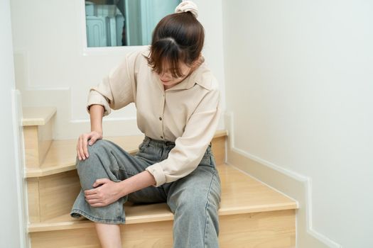 Asian lady woman touch and feel pain her knee on the stairs at home, healthy medical concept.