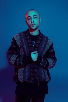 Close-up studio shot of a handsome tattoed bald male with a pirsing ring in his nose, wearing dark jacket, black trendy t-shirt with print, looking at the camera and posing against a colorful background with copy space. People, style and fashion concept. 90s style