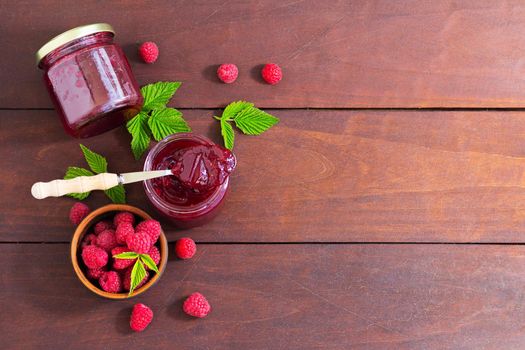 fresh raspberry jam in a glass jar on a wooden table, next to fresh raspberries. concept of homemade jam, preserves for winter, selective focus and copy space