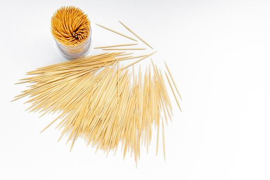 Pile of round wooden toothpicks and toothpick box with a plastic cover on white background. Copy space. Directly above. Flat lay.