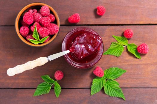 fresh raspberry jam in a glass jar on a wooden table, next to fresh raspberries. concept of homemade jam, preserves for winter, selective focus.