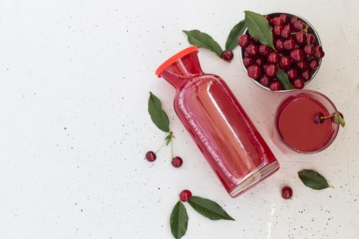 Cold cherry juice in a glass and bottle with ripe berries. Top view, copy space for text. The concept of summer refreshing drink morse or kompot.