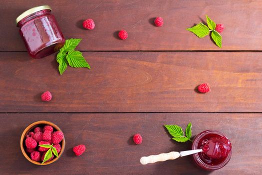 fresh raspberry jam in a glass jar on a wooden table, next to fresh raspberries. concept of homemade jam, preserves for winter, selective focus and copy space