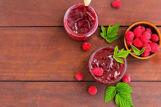 fresh raspberry jam in a glass jar on a wooden table, next to fresh raspberries. concept of homemade jam, preserves for winter, selective focus and copy space