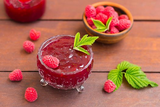 fresh raspberry jam in a glass jar on a wooden table, next to fresh raspberries. concept of homemade jam, preserves for winter, selective focus.