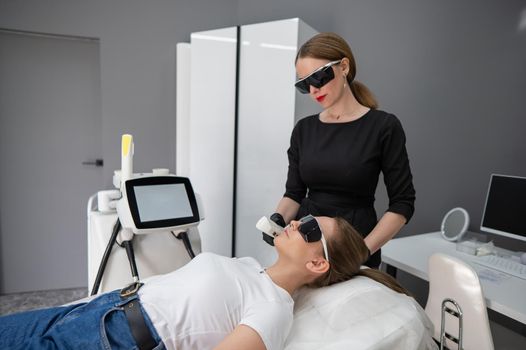 Young caucasian woman in goggles on photorejuvenation procedure. Doctor cosmetologist with a female patient