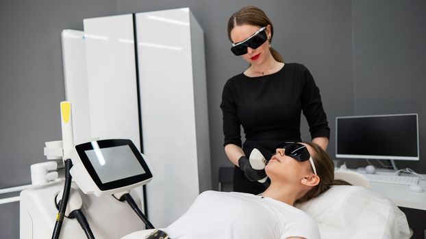 Young caucasian woman in goggles on photorejuvenation procedure. Doctor cosmetologist with a female patient