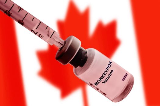 Monkeypox vaccine with a syringe close-up against the blurred national flag of Canada.