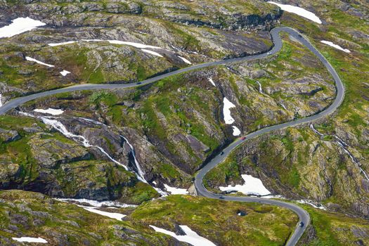 Winding road in a green landscape with snow patches seen in Norway