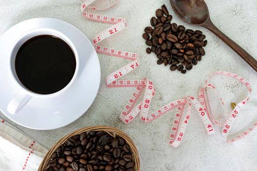 Cup of coffee and coffee beans background with measure tap on white desk. Beverage and diet concept. Directly above. Flat lay. Copy space.