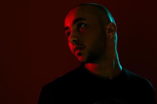 Close-up studio shot of a good-looking tattoed bald guy with a pirsing ring in his nose, wearing black trendy t-shirt with print, posing and looking up against a red background with copy space. People, style and fashion concept. 90s style