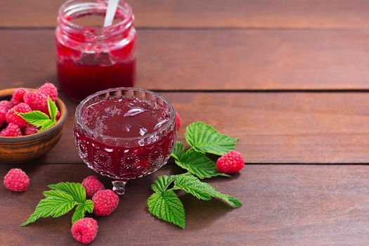 fresh raspberry jam in a glass jar on a wooden table, next to fresh raspberries. concept of homemade jam, preserves for winter, selective focus and copy space