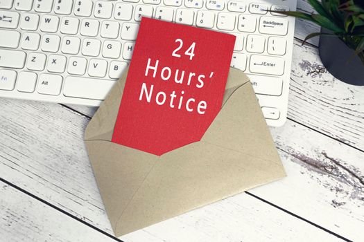 24 hours notice text on red note inside brown envelope with keyboard and potted plant background on wooden desk.