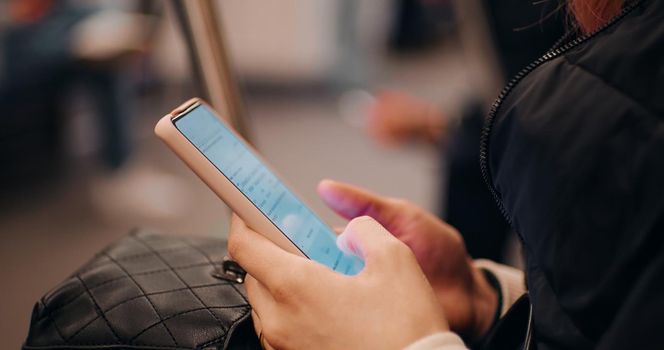 Close up of woman hands scrolling smartphone in public transport. Female hands sufing for information online. Technology concept.