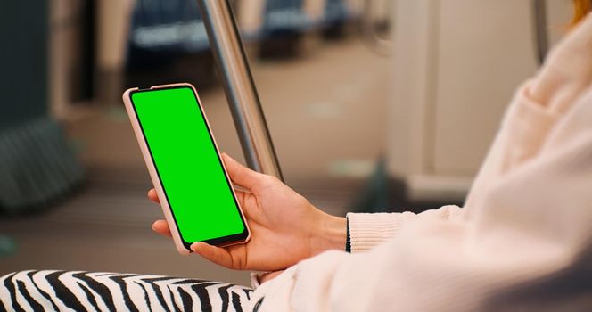 Woman hands using Smartphone with Green Screen display on train. Female hands watching film on a train. Technology era. Close-up hand holding Smartphone with Green Screen Mock Up.