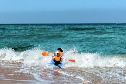 Two girls on a kayak are trying to swim out of a large oncoming coastal wave.