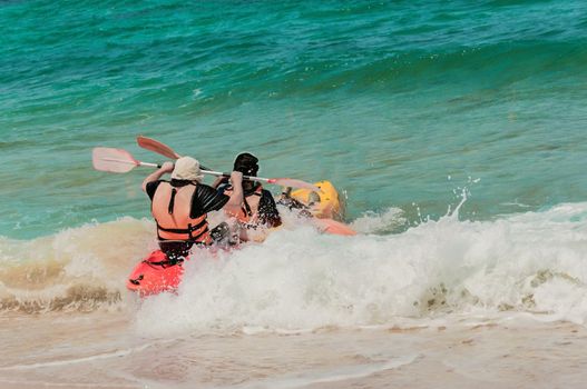 Two athletes compete in a kayak with sea waves, trying to swim away from the shore and not roll over