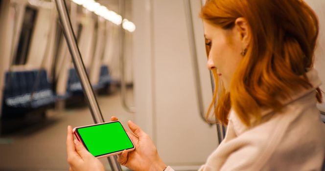 Horizontal Green Screen smartphone hold by woman, watching webinar online on underground transport. Apps. Technology. Cell Phone. Copyspace on phone.