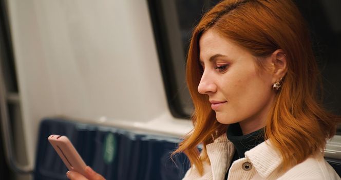 Woman browsing social media news, reading on smartphone screen, standing in public transport. Female surfing for information. Internet addiction.