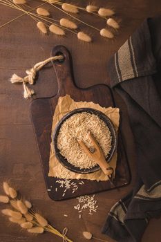 Brown rice in ceramic bowl with wooden scoop on rustic countertop.