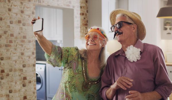 Say cheese. a happy senior couple standing together in costume and using a cellphone to take selfies