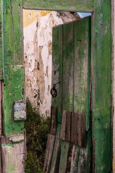 Open wooden green door to an abandoned overgrown building with a destroyed roof