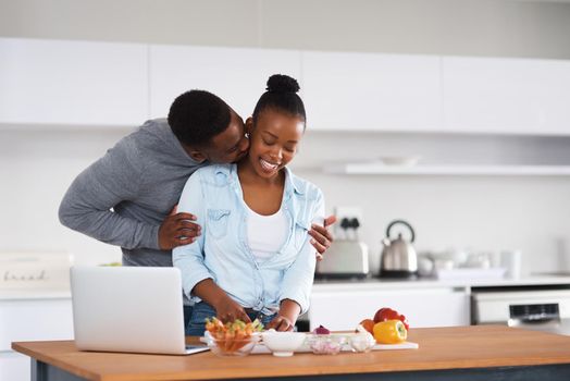 Kisses for the one who holds my heart. a man embracing his wife from behind while shes with chopping vegetables