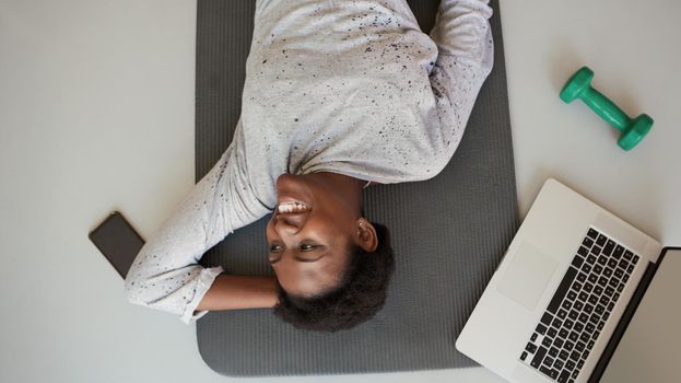 Be active, be healthy, be happy. High angle shot of a young woman lying on an exercise mat with a laptop, cellphone and dumbbell around her