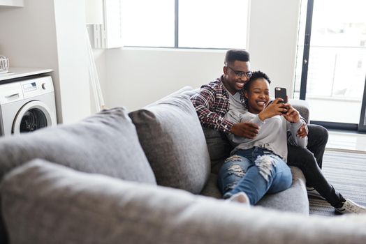 Scrolling through all the funny memes. a young couple using a cellphone while relaxing on a sofa at home