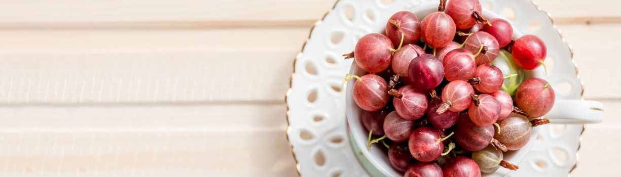 Fresh, sweet red gooseberries in a white cup on a white background.