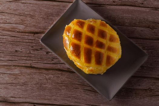 cream-filled bun covered with sugar syrup on a blue plate on a wooden table