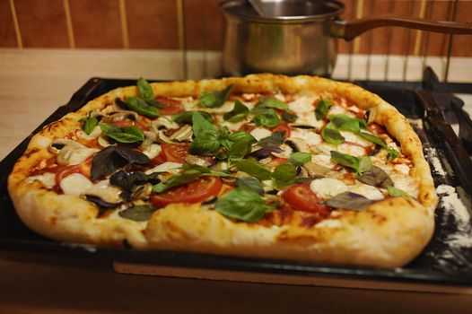 Homemade, freshly baked, appetizing Italian pizza with mozzarella and sides stuffed with salted feta cheese, juicy tomatoes, mushrooms and basil leaves on baking sheet. Close-up Culinary. Healthy food