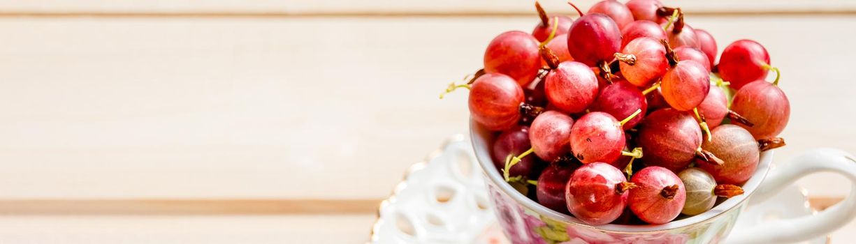 Fresh, sweet red gooseberries in a white cup on a white background.