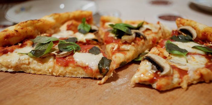 Slices of freshly baked homemade Italian pizza with mozzarella cheese and feta in the sides, just taken out from an oven and served on a wooden board