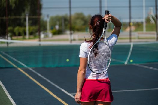 Woman in skirt standing back on the tennis court and holds the racket