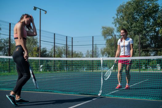 Two athletic young women play tennis on an outdoor court on a hot summer day